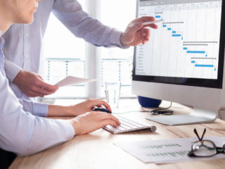 Project management team updating schedule or planning on computer, business